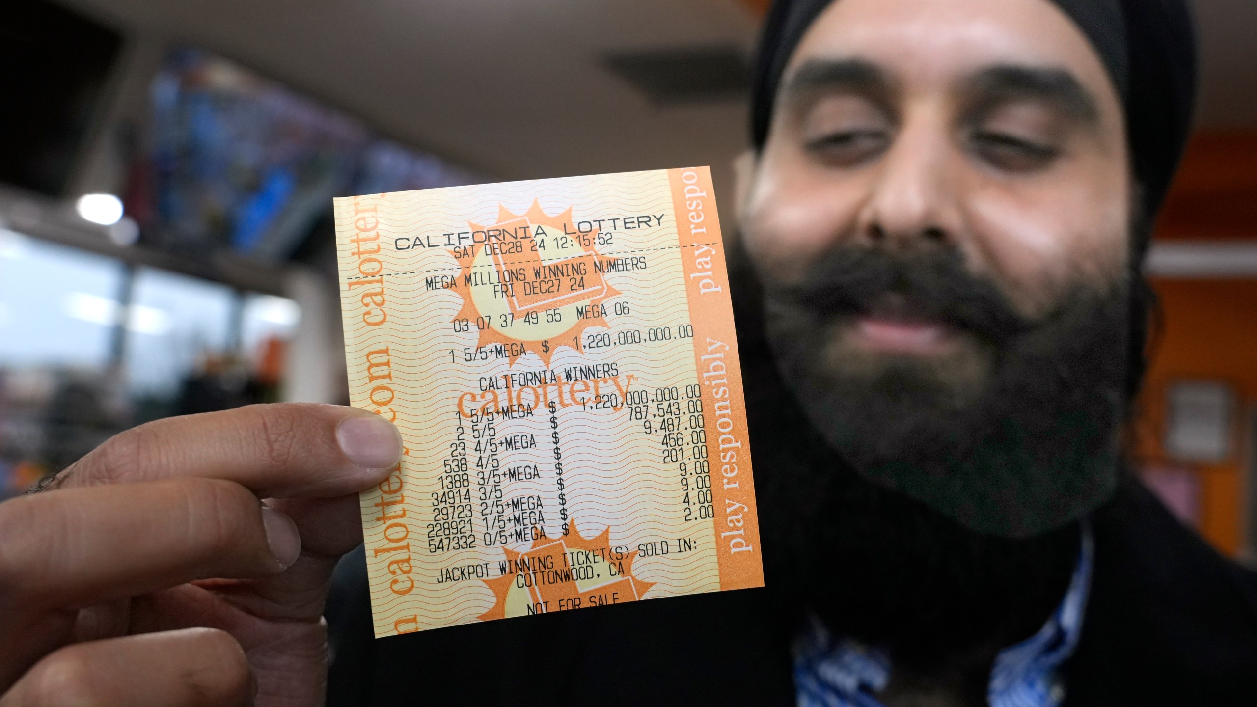 Ishar Gill holds up a copy of the Mega Millions lotto ticket worth an estimated $1.22 billion at his family's store in Cottonwood, Calif., Saturday, Dec. 28, 2024. After three months without anyone winning the top prize in the lottery, the ticket with the winning numbers was drawn Friday night.(AP Photo/Rich Pedroncelli).