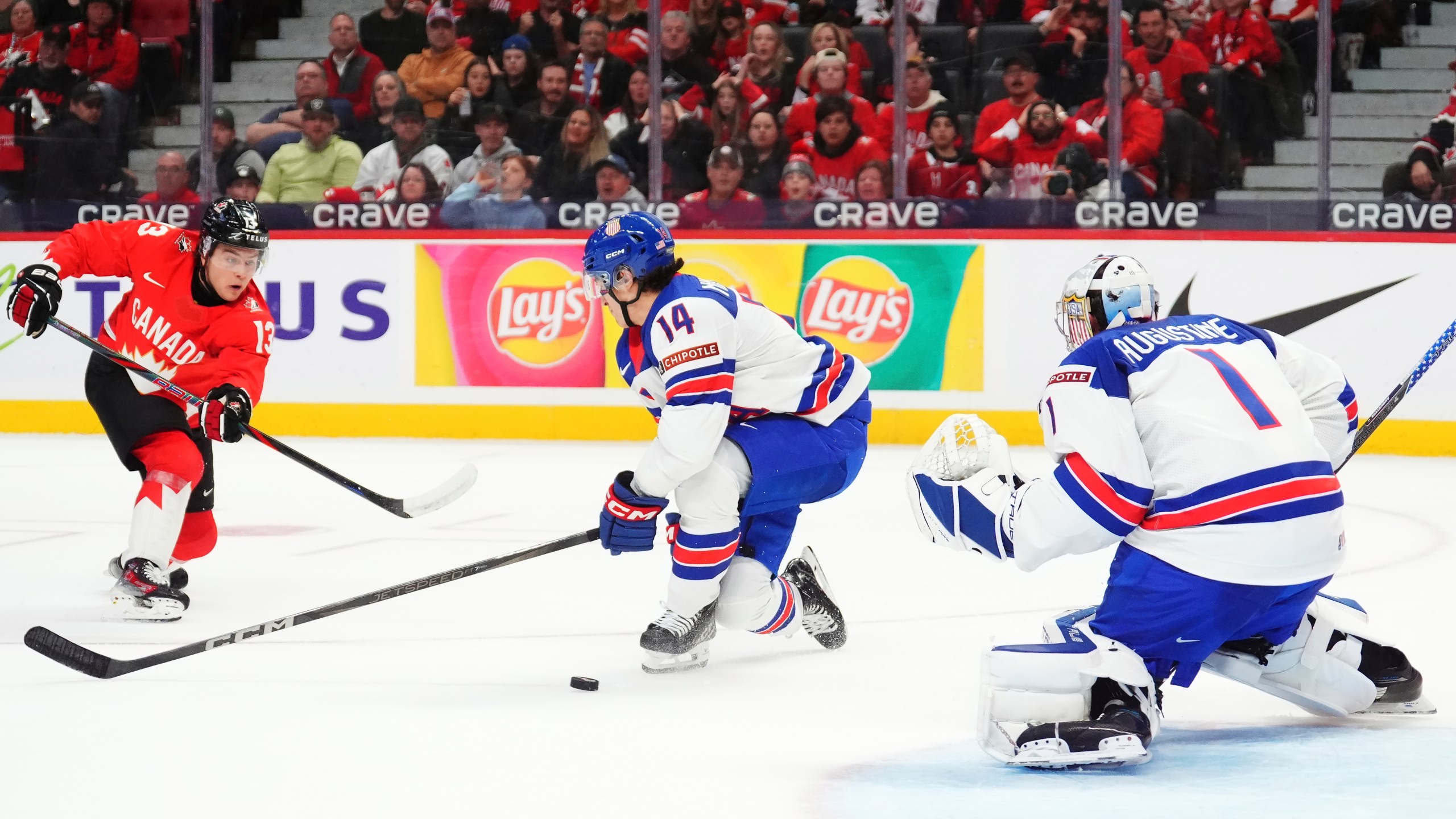 Canada's Luca Pinelli (13) shoots against United States goaltender Trey Augustine (1) as United States' Aram Minnetian (14) defends during second-period IIHF World Junior Hockey Championship tournament game action in Ottawa, Ontario, Tuesday, Dec. 31, 2024. (Sean Kilpatrick/The Canadian Press via AP)