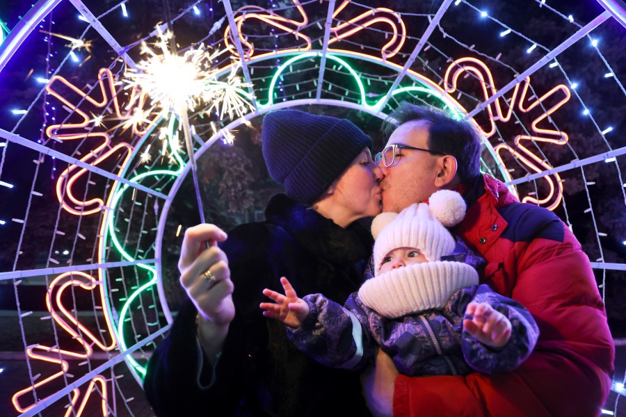 A couple kisses as they walk with their child in a square decorated for Christmas and the New Year festivities in Donetsk in Russian-controlled Donetsk region, eastern Ukraine, Tuesday, Dec. 31, 2024. (AP Photo/Alexei Alexandrov)