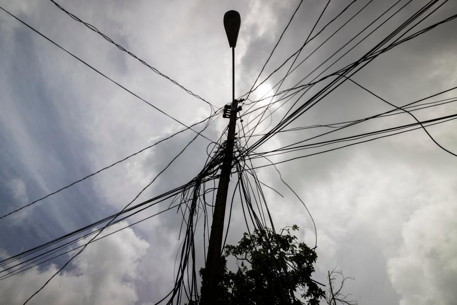 FILE - A utility pole with loose cables towers over a home in Loiza, Puerto Rico, Sept. 15, 2022. (AP Photo/Alejandro Granadillo, File)