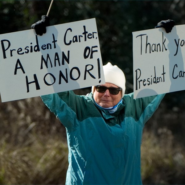 A person holds signs as the hearse containing the casket of former President Jimmy Carter, pauses at the Jimmy Carter Boyhood Farm in Archery, Ga., Saturday, Jan. 4, 2025. Carter died Dec. 29 at the age of 100. (AP Photo/Alex Brandon, Pool)