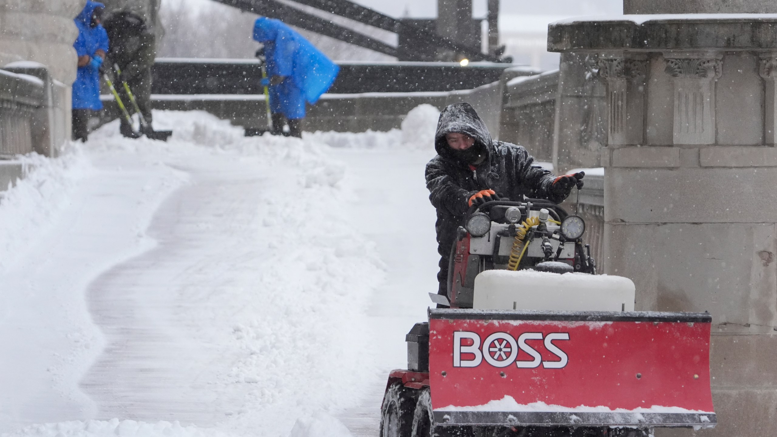 Workers clear snow from a walkway Sunday, Jan. 5, 2025, in St. Louis. (AP Photo/Jeff Roberson)