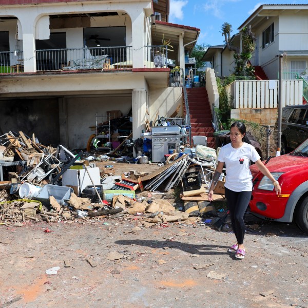 A woman walks in front of the home where a New Year's Eve fireworks explosion killed and injured people, Wednesday, Jan. 1, 2025, in Honolulu. (AP Photo/Marco Garcia)