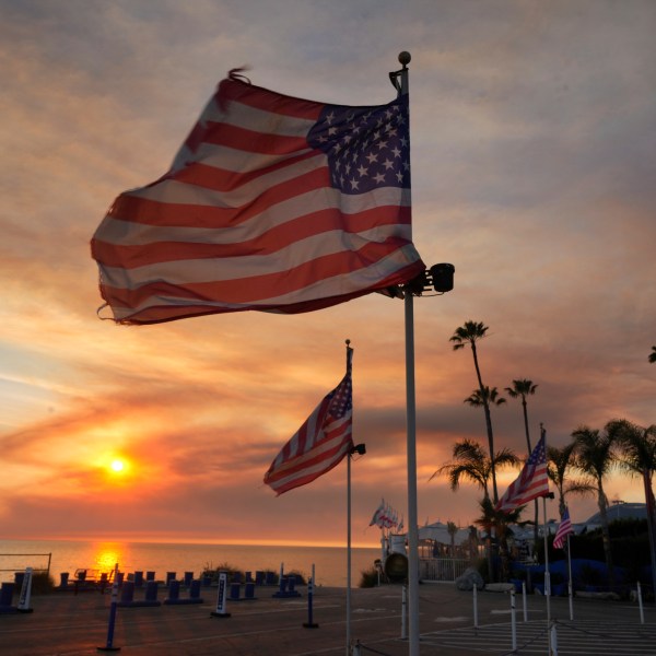 FILE - Flags fly under heavy winds before sunset as a plume of smoke from the Franklin Fire rises over the ocean Tuesday, Dec. 10, 2024, in Malibu, Calif. (AP Photo/Damian Dovarganes,File)