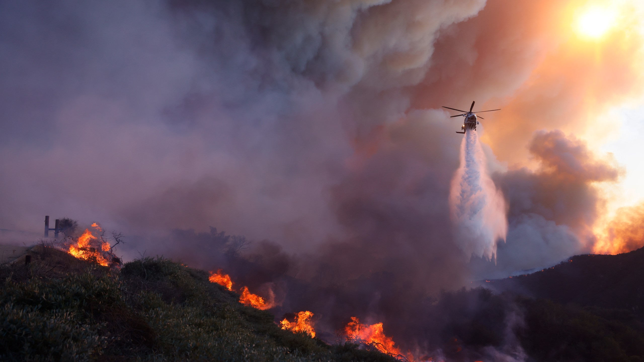 Water is dropped by helicopter on the advancing Palisades Fire in the Pacific Palisades neighborhood of Los Angeles, Tuesday, Jan. 7, 2025. (AP Photo/Etienne Laurent)