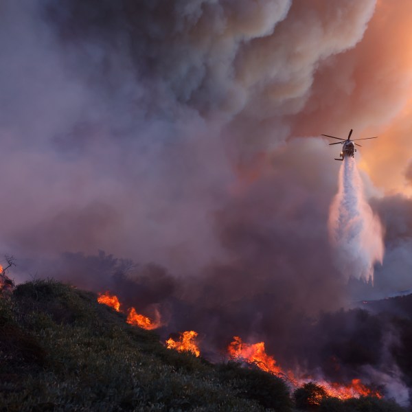 Water is dropped by helicopter on the advancing Palisades Fire in the Pacific Palisades neighborhood of Los Angeles, Tuesday, Jan. 7, 2025. (AP Photo/Etienne Laurent)