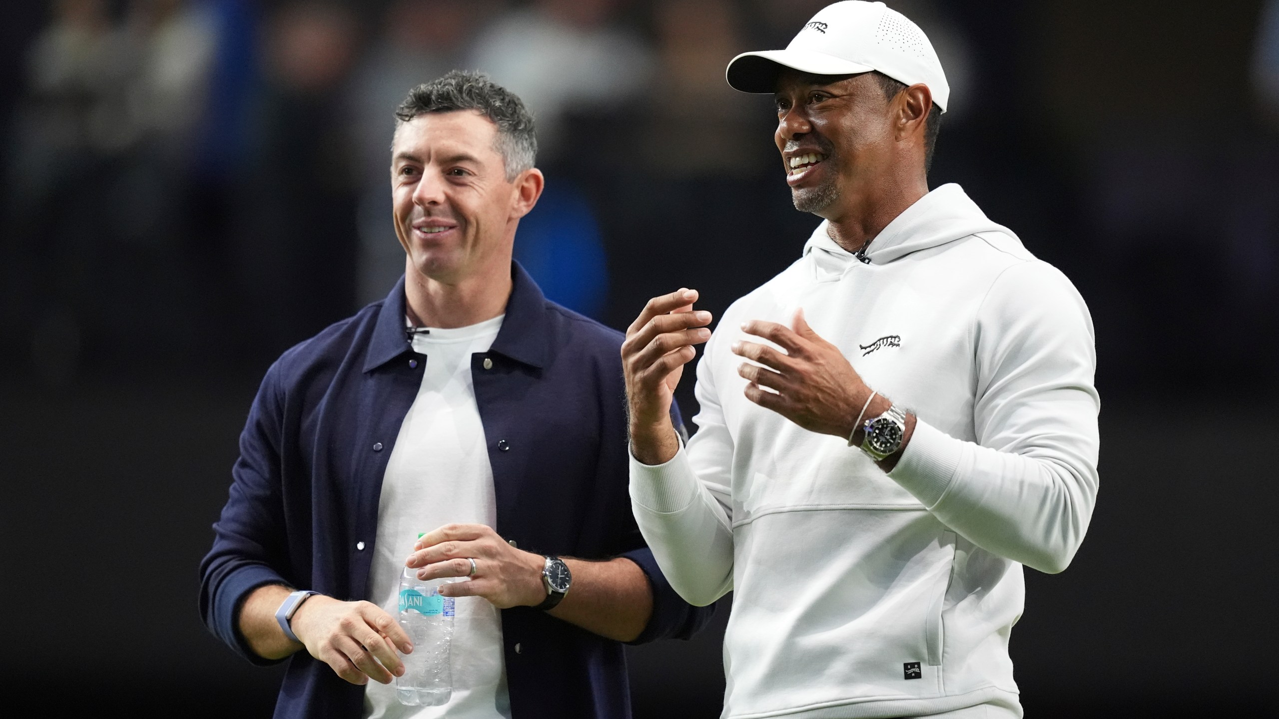 Rory McIlroy and Tiger Woods stand on the green as they watch New York Golf Club and The Bay Golf Club warmup for the inaugural match of the TMRW Golf League, Tuesday, Jan. 7, 2025, in Palm Beach Gardens, Fla. TGL features six teams of four players competing against each other in a tech-infused arena the size of a football field. (AP Photo/Rebecca Blackwell)