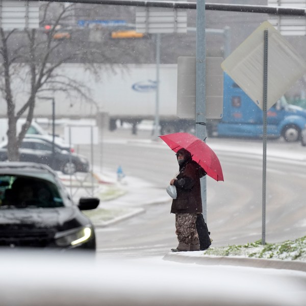 A man who gave his name as Servo uses an umbrella to cross a street as snow falls Thursday, Jan. 9, 2025, in Dallas. (AP Photo/LM Otero)