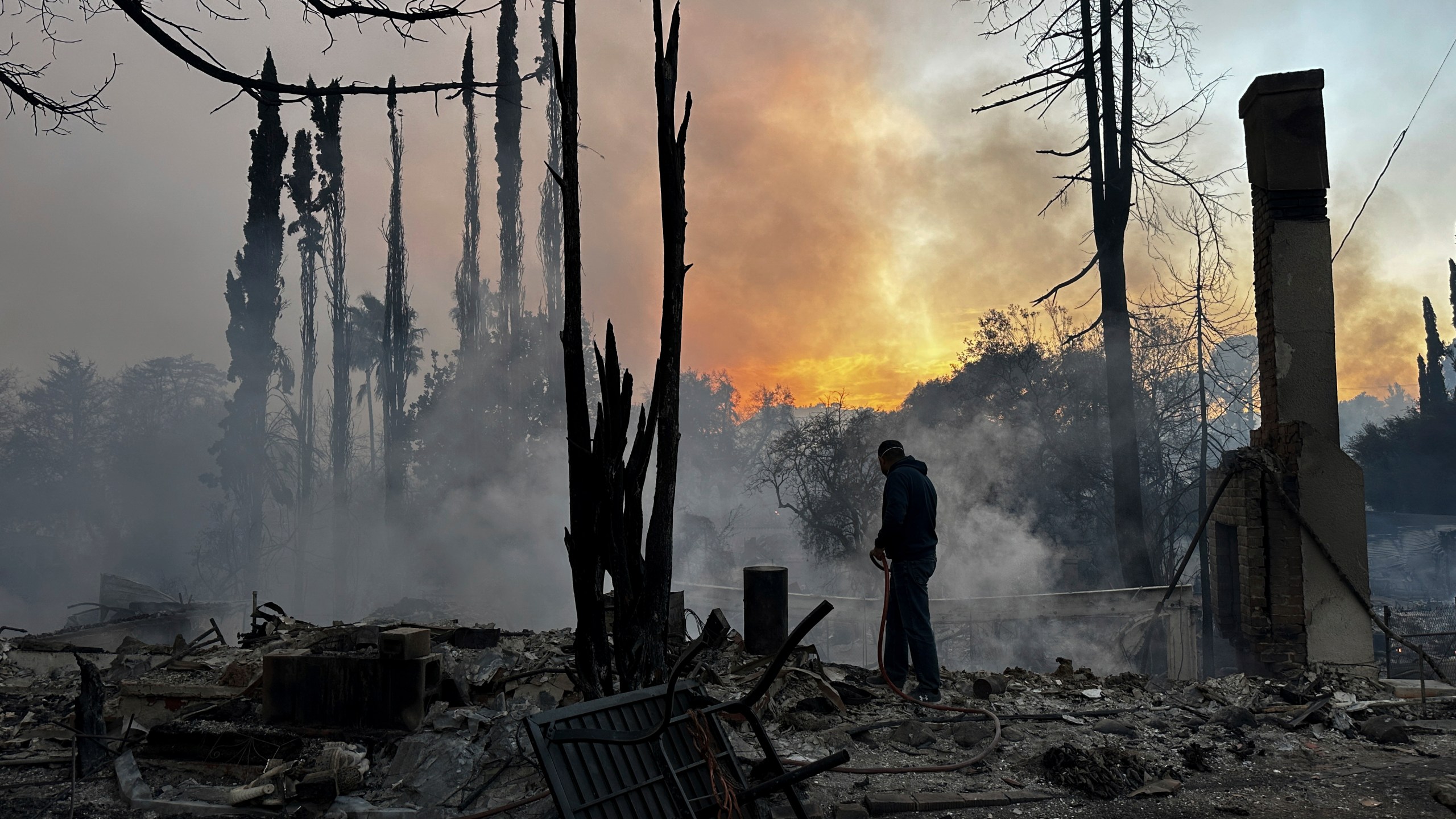 A resident hoses down hot spots in a fire-ravaged property after the Palisades Fire swept through in the Pacific Palisades neighborhood of Los Angeles, Wednesday, Jan. 8, 2025. (AP Photo/Eugene Garcia)