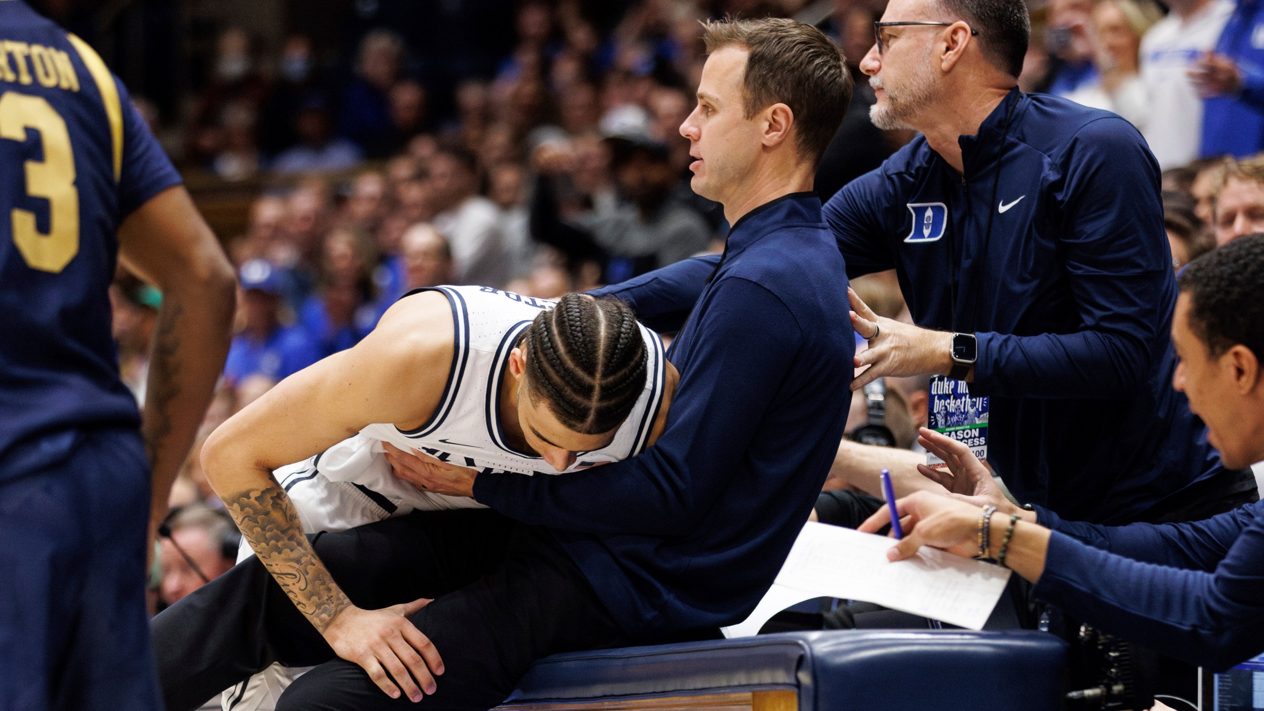 Duke's Tyrese Proctor, left, falls into Duke head coach Jon Scheyer, right, after chasing a loose ball during the first half of an NCAA college basketball game against Notre Dame in Durham, N.C., Saturday, Jan. 11, 2025. (AP Photo/Ben McKeown)