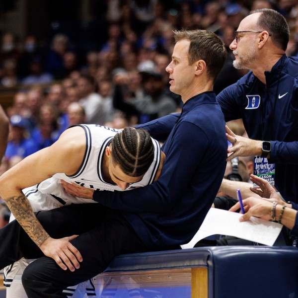 Duke's Tyrese Proctor, left, falls into Duke head coach Jon Scheyer, right, after chasing a loose ball during the first half of an NCAA college basketball game against Notre Dame in Durham, N.C., Saturday, Jan. 11, 2025. (AP Photo/Ben McKeown)