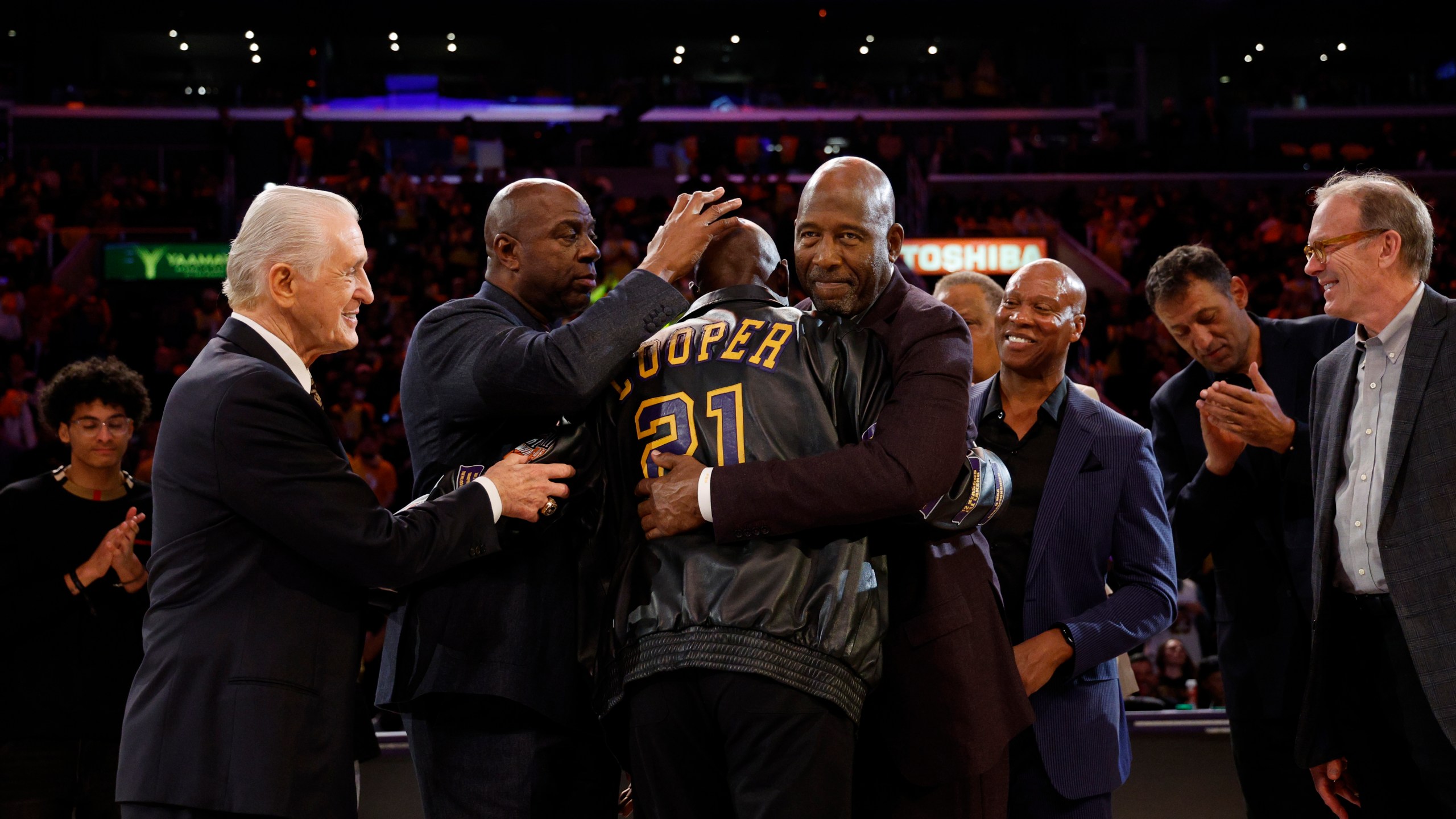 Former Los Angeles Lakers player Michel Cooper, center, is mobbed by coach Pat Riley, left, Magic Johnson, James Worthy, Byron Scott, Vlade Divac and Kurt Rambis after his jersey was retired during a ceremony during halftime in an NBA basketball game between the Lakers and the San Antonio Spurs, Monday, Jan. 13, 2025, in Los Angeles. (AP Photo/Kevork Djansezian)