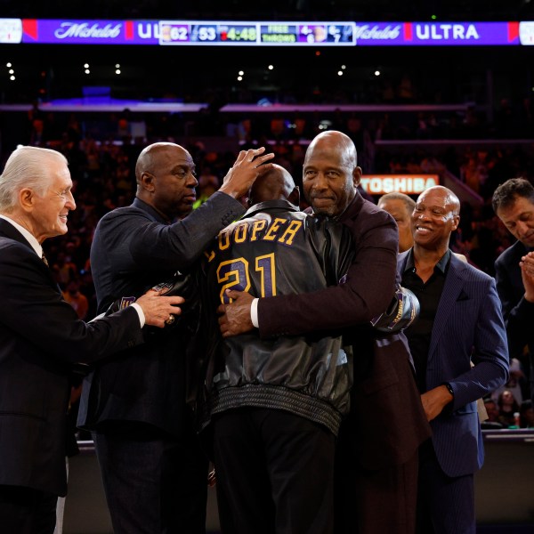 Former Los Angeles Lakers player Michel Cooper, center, is mobbed by coach Pat Riley, left, Magic Johnson, James Worthy, Byron Scott, Vlade Divac and Kurt Rambis after his jersey was retired during a ceremony during halftime in an NBA basketball game between the Lakers and the San Antonio Spurs, Monday, Jan. 13, 2025, in Los Angeles. (AP Photo/Kevork Djansezian)