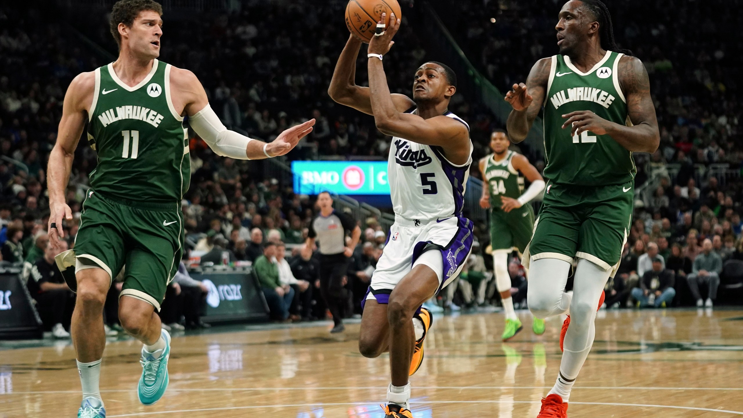 Sacramento Kings' De'Aaron Fox (5) drives to the basket between Milwaukee Bucks' Brook Lopez (11) and Taurean Prince during the first half of an NBA basketball game, Tuesday, Jan. 14, 2025, in Milwaukee. (AP Photo/Aaron Gash)