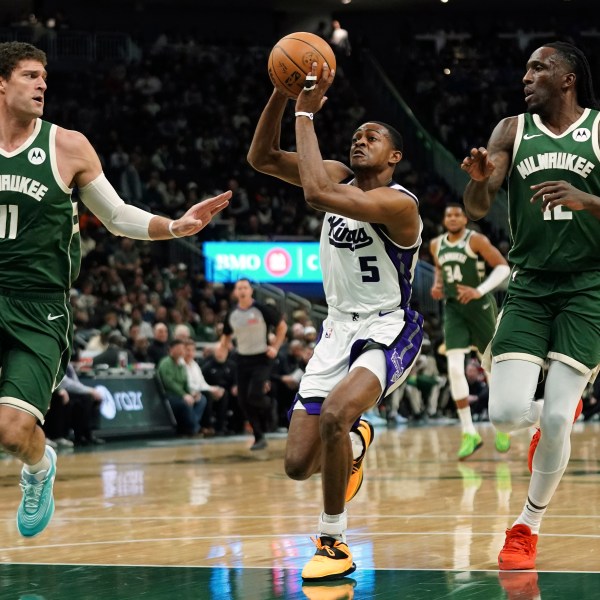 Sacramento Kings' De'Aaron Fox (5) drives to the basket between Milwaukee Bucks' Brook Lopez (11) and Taurean Prince during the first half of an NBA basketball game, Tuesday, Jan. 14, 2025, in Milwaukee. (AP Photo/Aaron Gash)