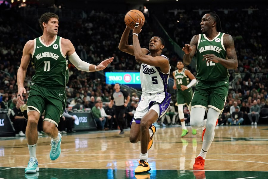 Sacramento Kings' De'Aaron Fox (5) drives to the basket between Milwaukee Bucks' Brook Lopez (11) and Taurean Prince during the first half of an NBA basketball game, Tuesday, Jan. 14, 2025, in Milwaukee. (AP Photo/Aaron Gash)