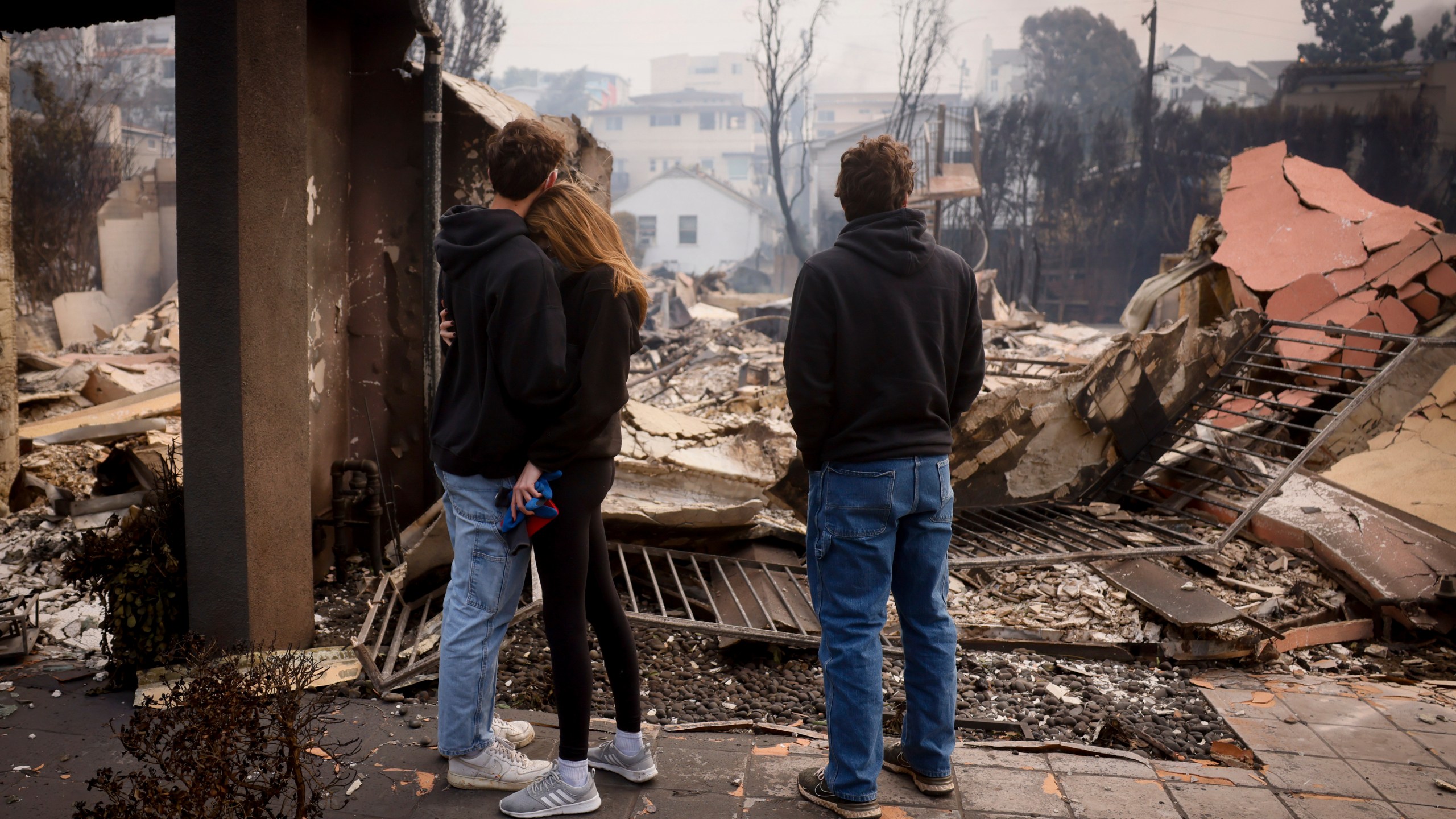 FILE - Residents embrace in front of a fire-ravaged property after the Palisades Fire swept through in the Pacific Palisades neighborhood of Los Angeles, Wednesday, Jan. 8, 2025. (AP Photo/Etienne Laurent, File)