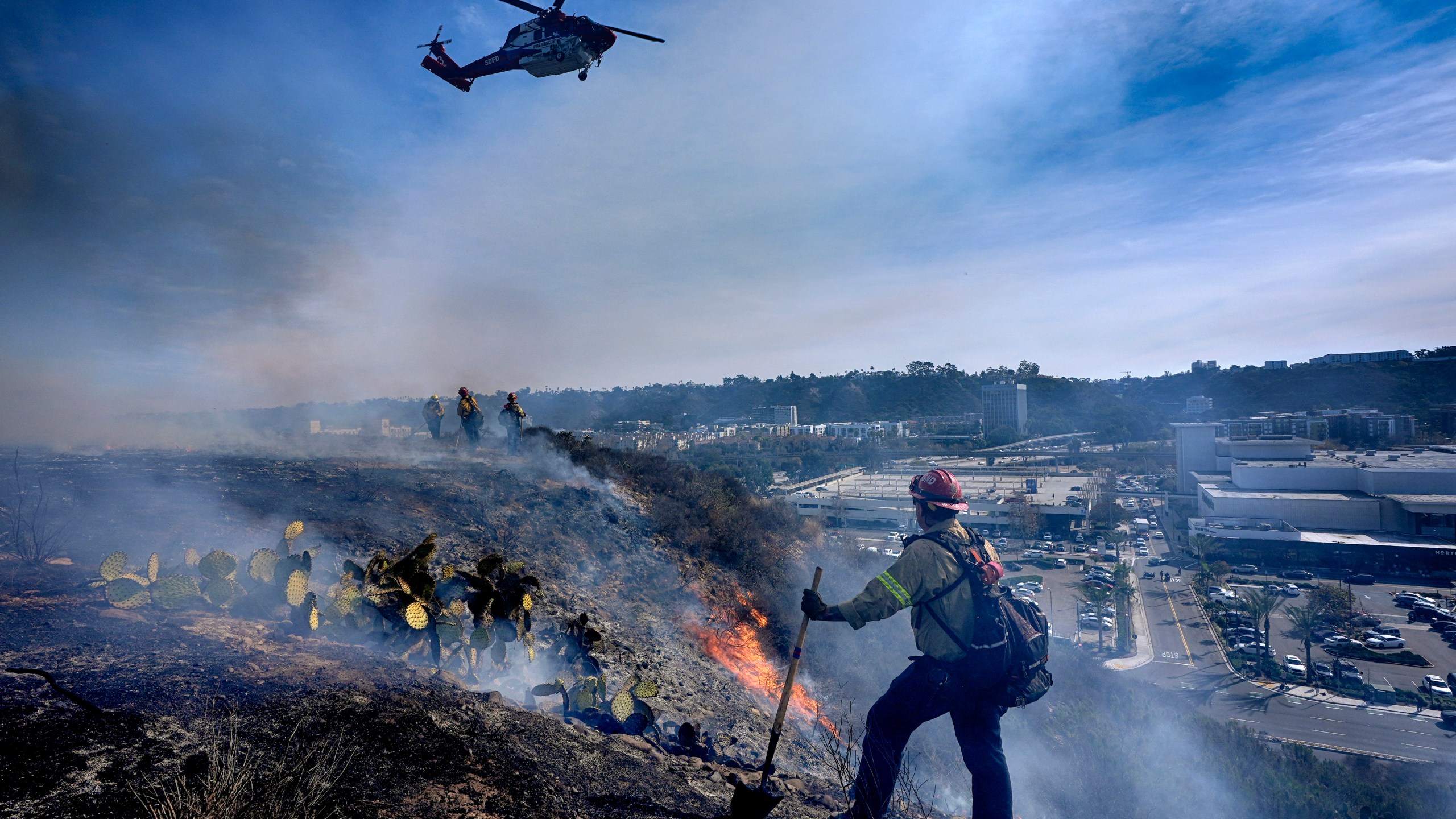 San Diego firefighters knock down a small brush along a hillside over the Mission Valley Shopping Mall in San Diego on Tuesday, Jan. 21, 2025. (AP Photo/Gregory Bull)