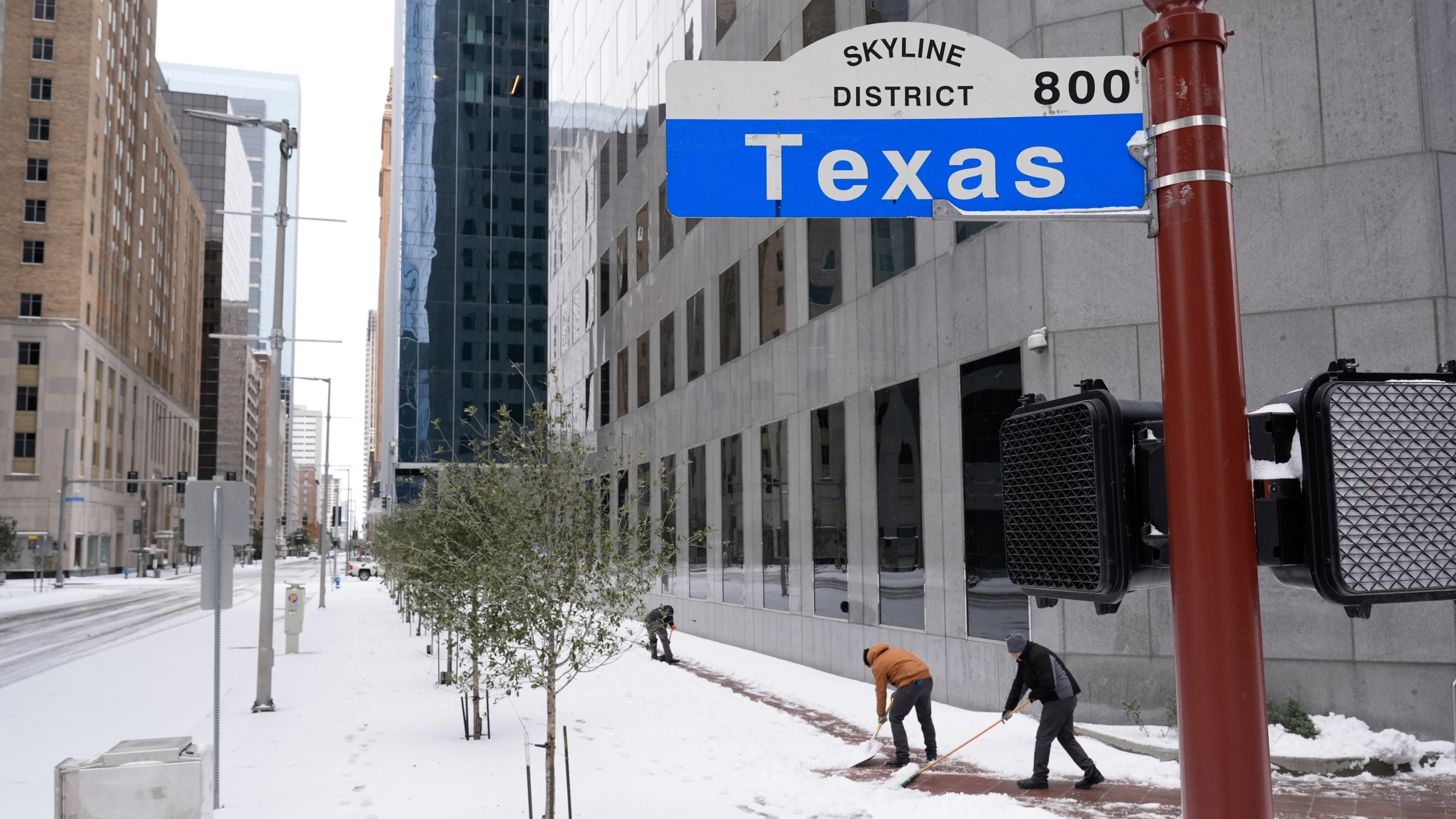 People shovel snow off the sidewalk Tuesday, Jan. 21, 2025, in downtown Houston. (AP Photo/Ashley Landis)