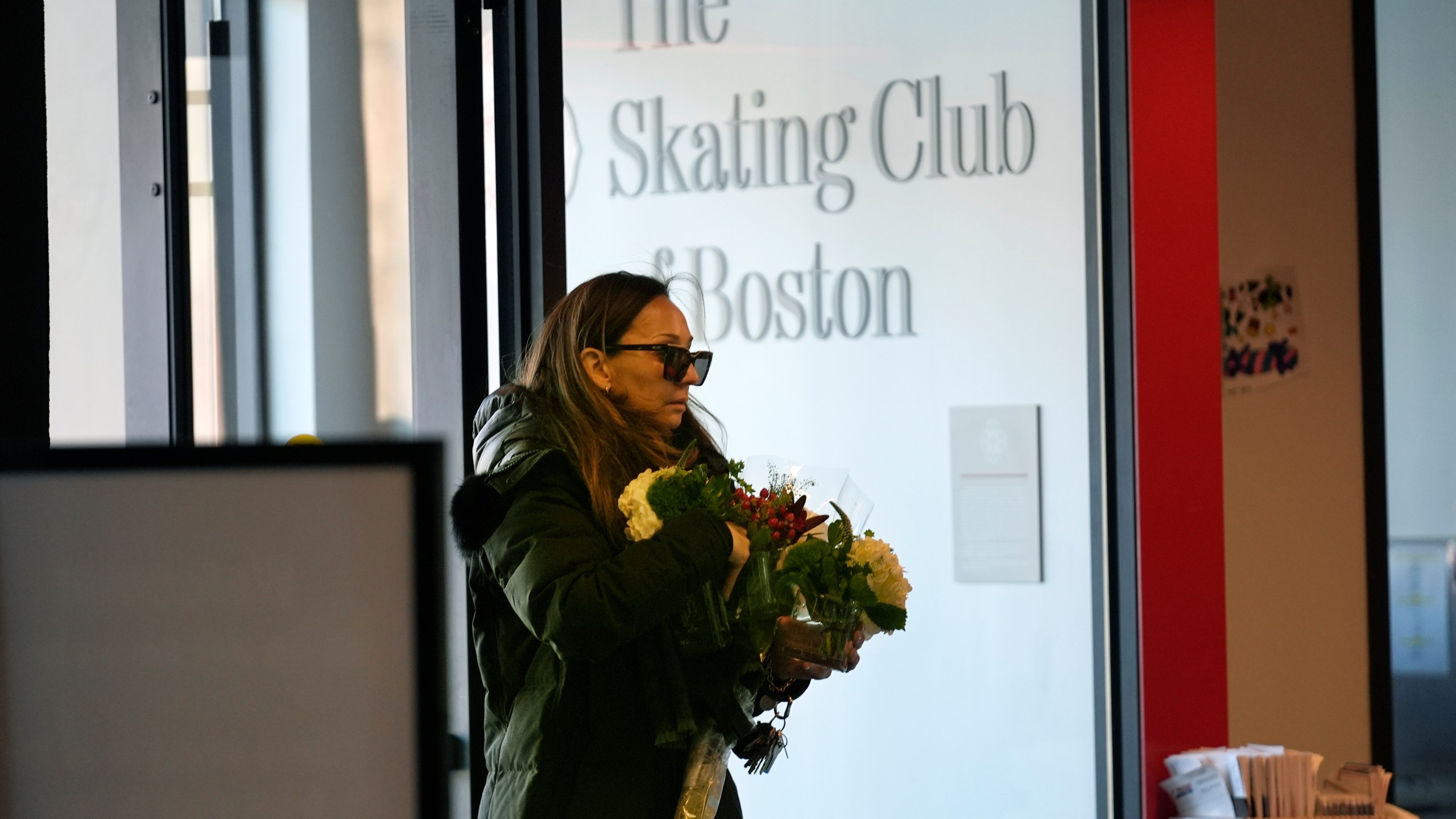 A woman brings flowers to The Skating Club of Boston, where six athletes, coaches and family associated with the club are believed to have perished in the collision of a passenger aircraft and military helicopter in Washington, Thursday, Jan. 30, 2025, in Norwood, Mass. (AP Photo/Robert F. Bukaty)