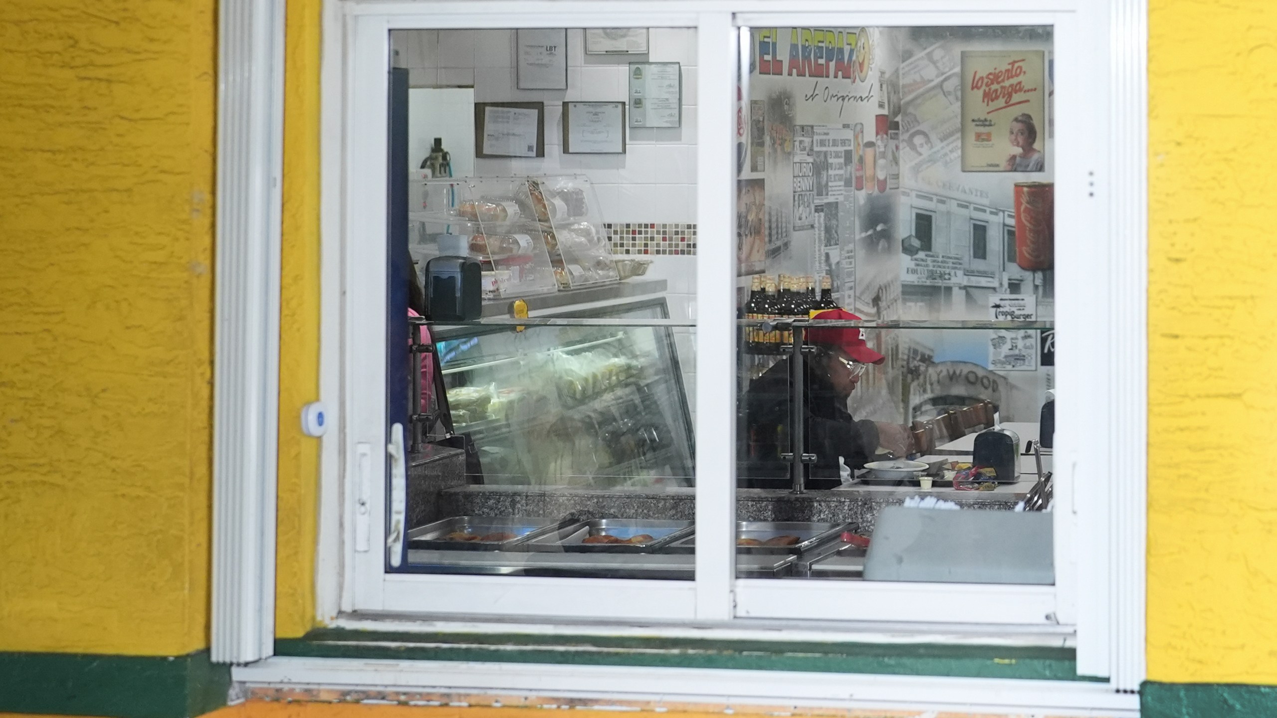 A patron of Venezuelan restaurant El Arepazo is seen through a window as Venezuelan community leaders gather outside for a press conference to denounce changes to the protections that shielded hundreds of thousands of Venezuelans from deportation, Monday, Feb. 3, 2025, in Doral, Fla. (AP Photo/Rebecca Blackwell)