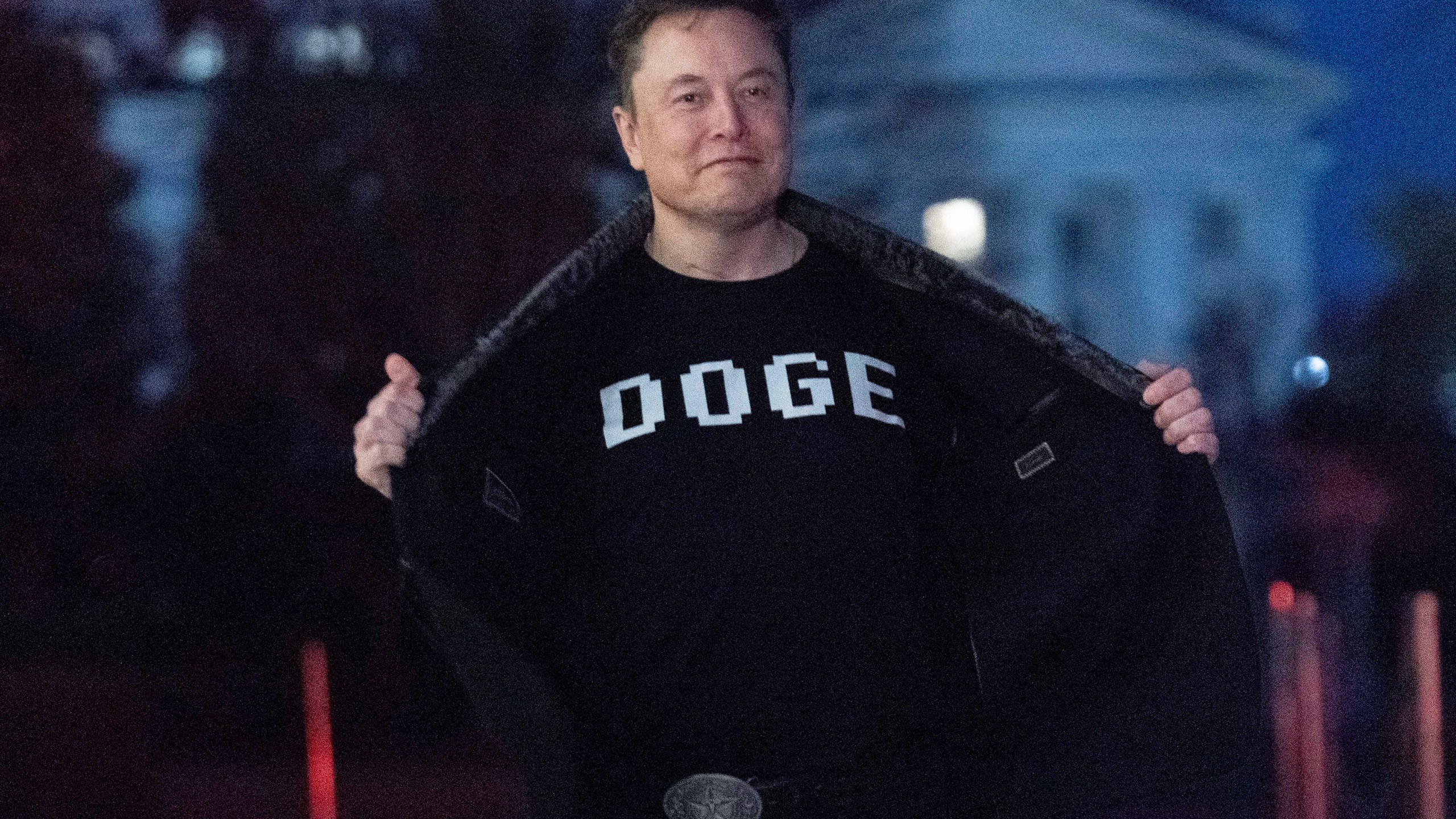 Elon Musk flashes his t-shirt that reads "DOGE" to the media as he walks on South Lawn of the White House, in Washington, Sunday, March 9, 2025. (AP Photo/Jose Luis Magana)